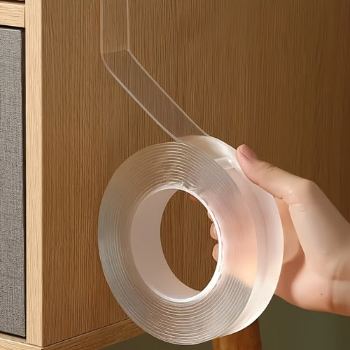 Hand holding a roll of clear tape against a wooden cabinet.