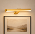 Gold wall light fixture on a beige wall with a framed landscape print below.