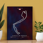 A formula 1 poster of the Monaco grand prix curcuit on a table with 2 plants next to it infront of a mustard colored wall.