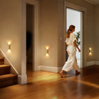 Woman walking into a well-lit room with wooden floors and wall sconces.