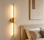 Modern wall sconce on a wall above a bed with abstract art in the background