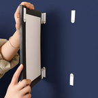 Person holding a black frame with small white hooks against a blue wall.