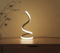 Modern spiral table lamp on a wooden surface with a plant in the background
